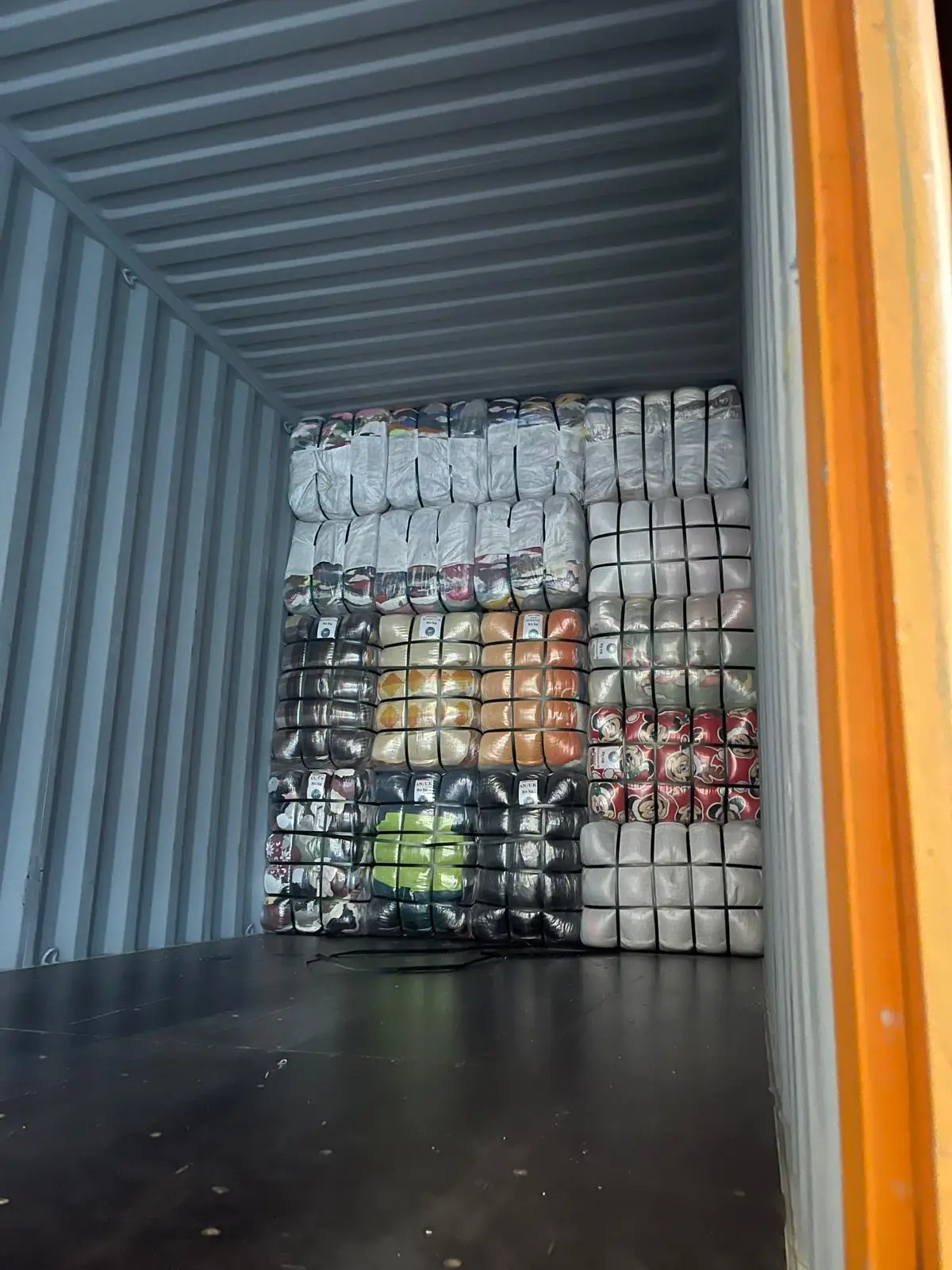 Container being loaded with different types of labelled clothing bales