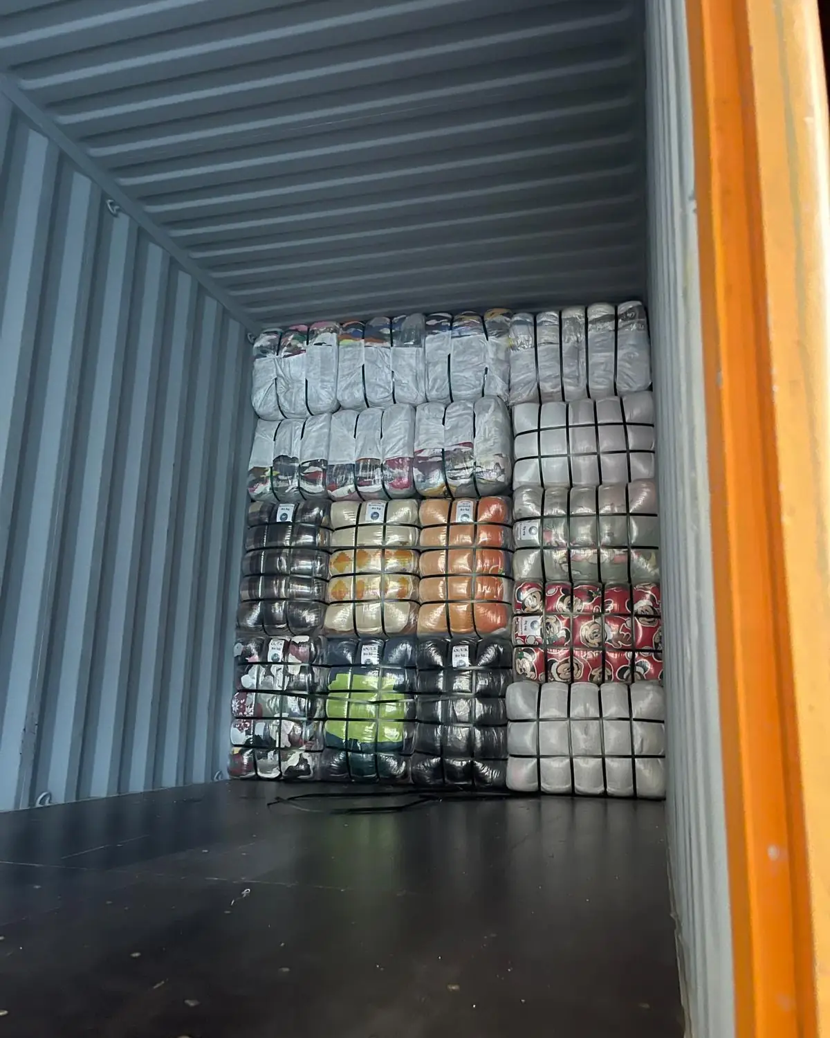 Container being loaded with different types of labelled clothing bales